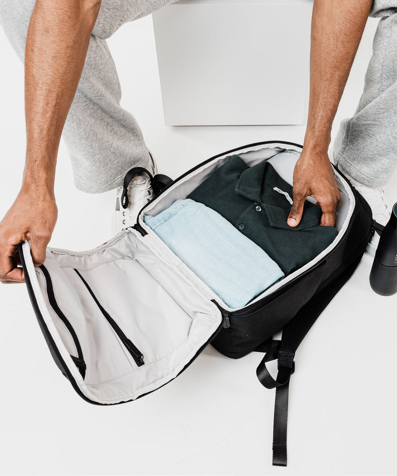 Person opening a black backpack with clothes inside on a white background